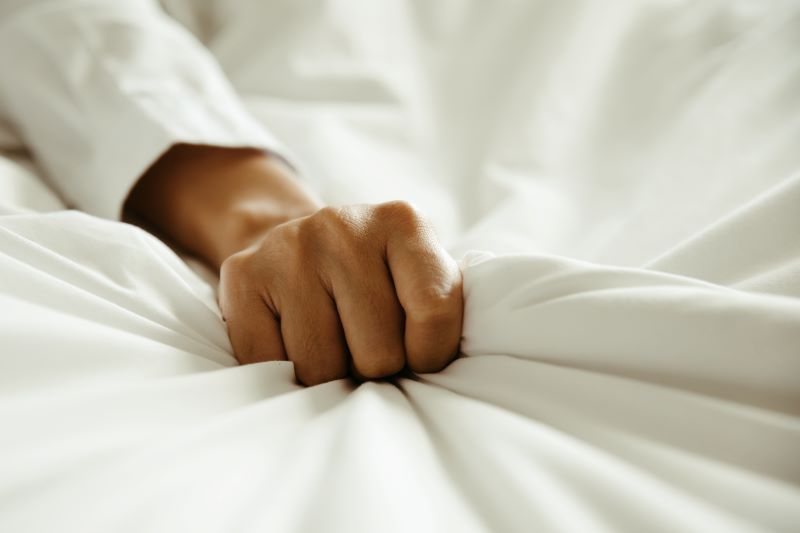 Close up of hand gripping bed sheets