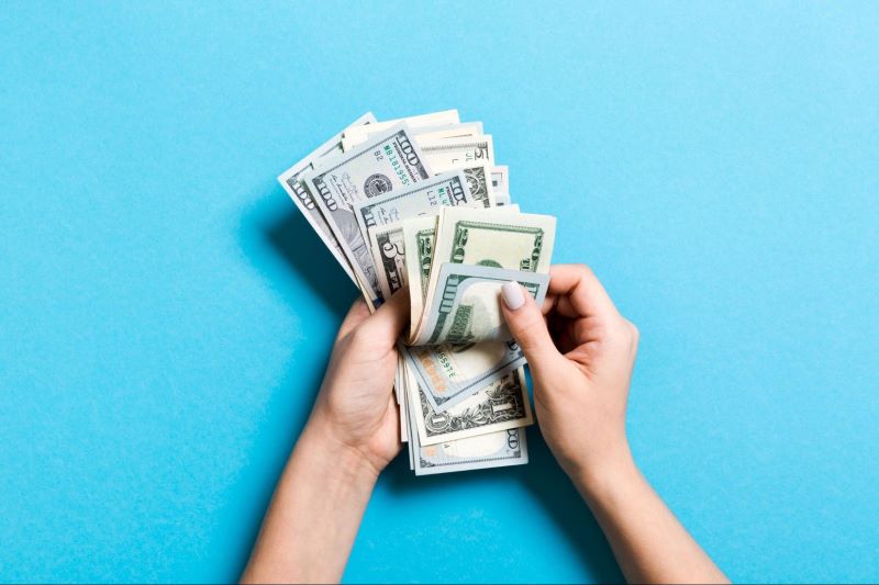 Hand counting dollar bills on blue background