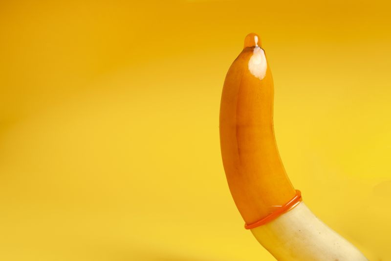 Banana with orange condom on yellow background