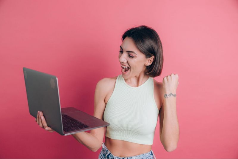Celebrating woman holding laptop on pink background