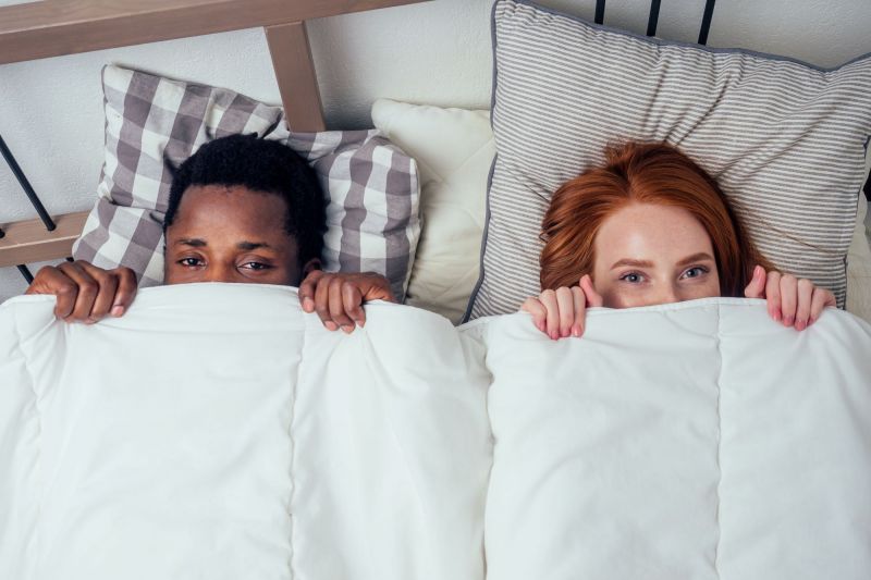 Cheeky couple hiding under bedsheets