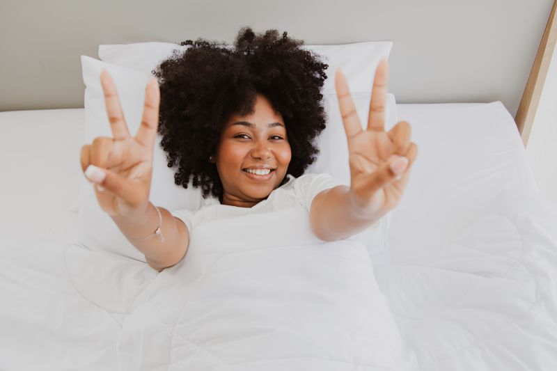 Cheerful woman making peace signs from white bed