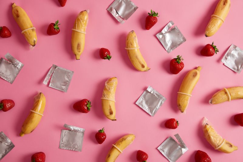 Condoms and fruit on pink background