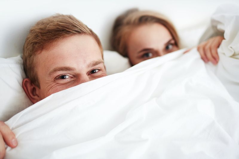 Couple in bed hiding under duvet