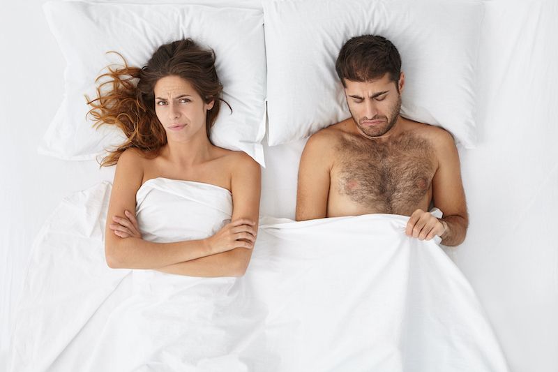 Couple in bed looking confused and unsatisfied