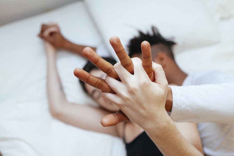 Couple in bed with close up of their hands entwined