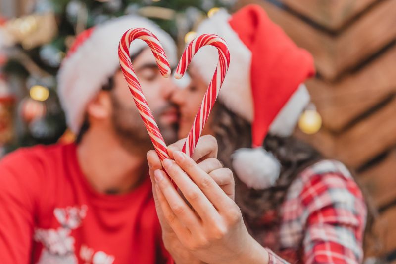 Couple s'embrasser dans des chapeaux de Père Noël avec un coeur de canne en bonbon
