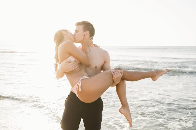 Couple kissing on the beach with man picking up girlfriend