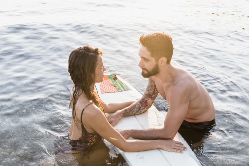 Couple smiling near surfboard in water