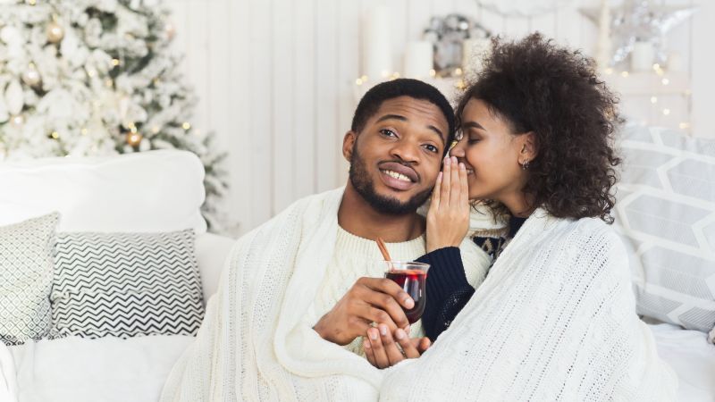 Couple chuchotant à la maison avec du vin chaud