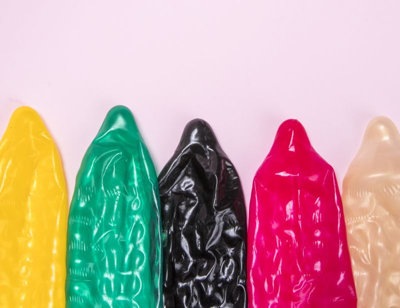 Different coloured condoms on pink background