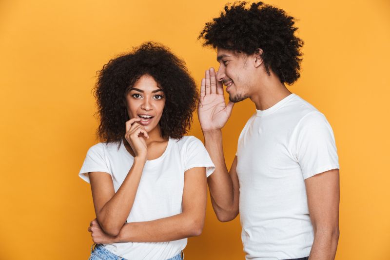 Excited couple sharing secrets on yellow background