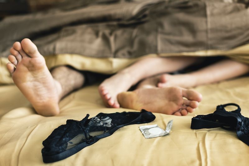 Les pieds du couple au lit à côté des préservatifs et de la lingerie