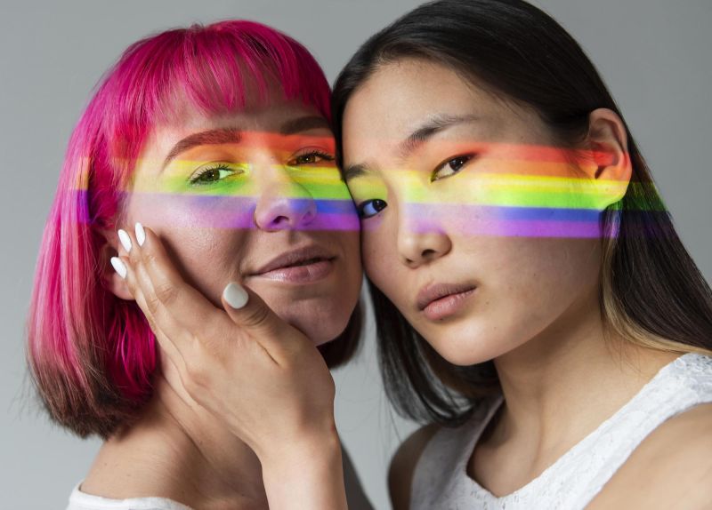 Queer couple with rainbow light across faces