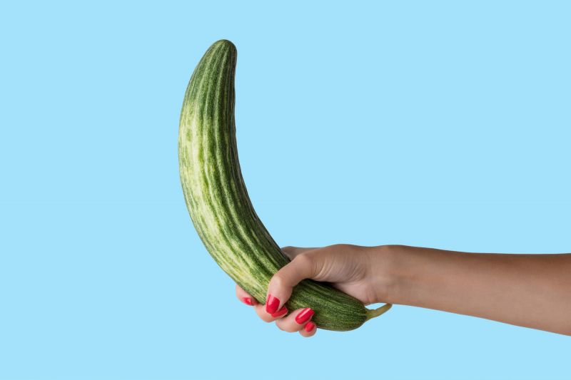 Female hand holding cucumber on blue background