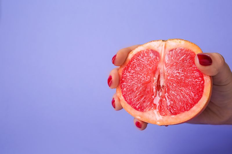 Hand squeezing grapefruit on purple background