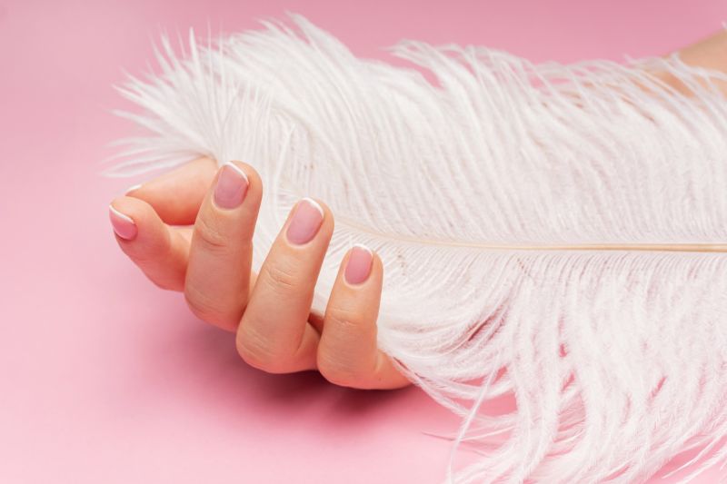 Female hand with white feather on pink background