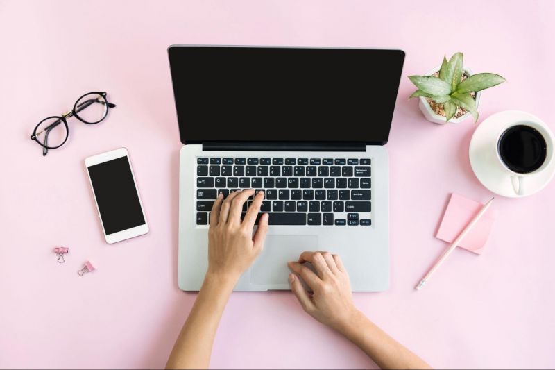 Female hands on laptop and pink workspace