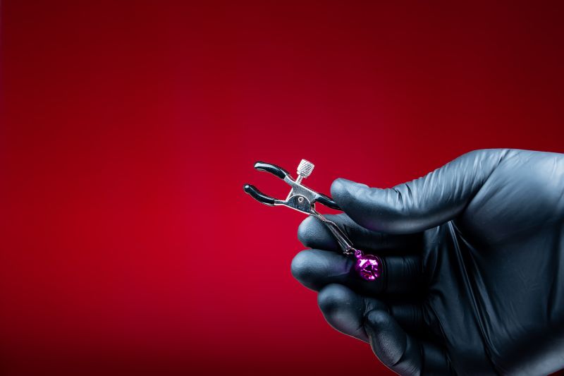 Black loved hand holding nipple clamp red background