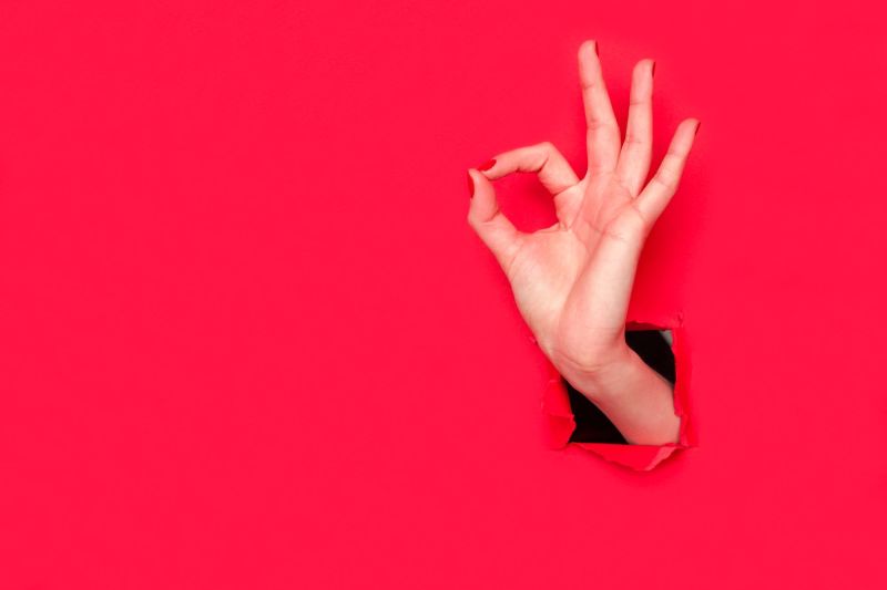 Hand doing okay sign on red background