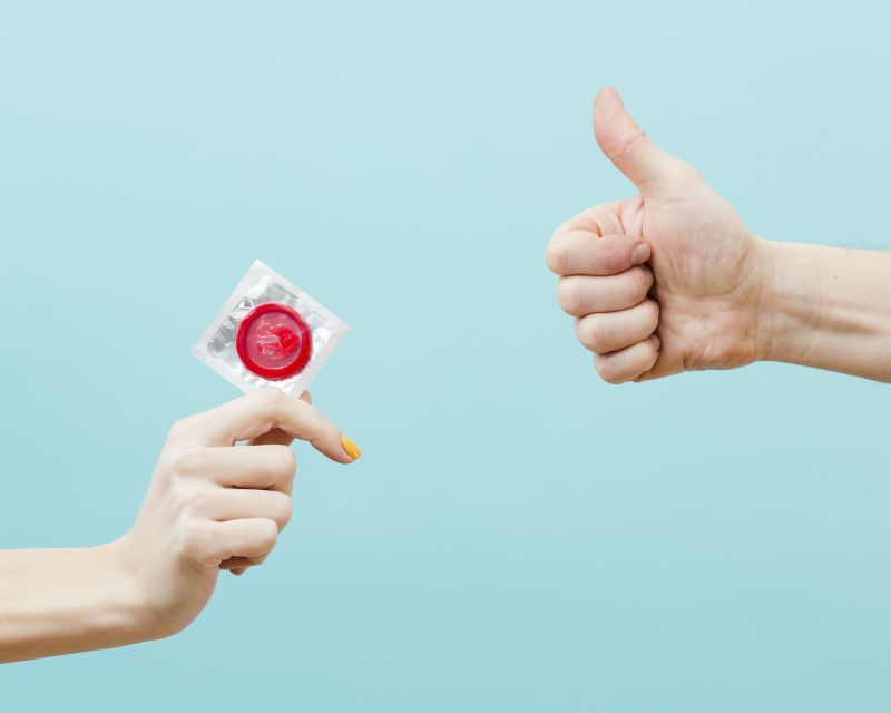 Hand holding condom and hand doing thumbs up