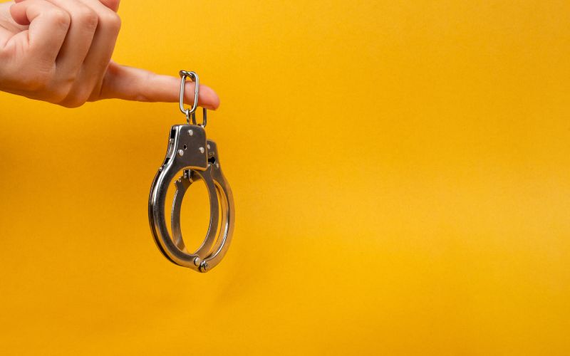 Hand holding handcuffs on yellow background