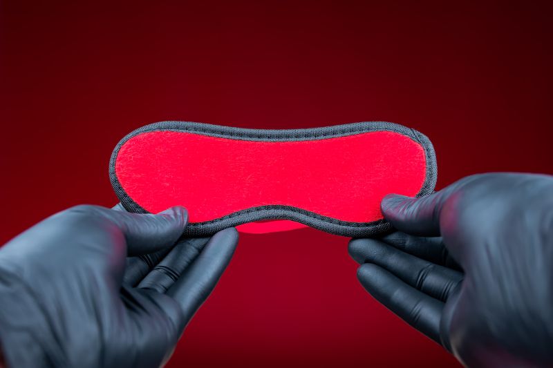 Mains dans des gants noirs tenant un masque pour les yeux érotique