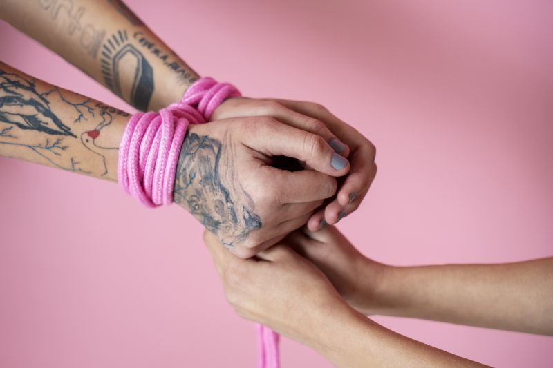 Tattooed hands wearing pink rope