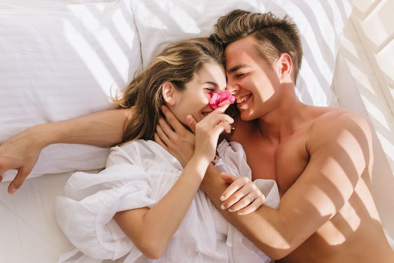 Happy couple laughing in bed in the morning