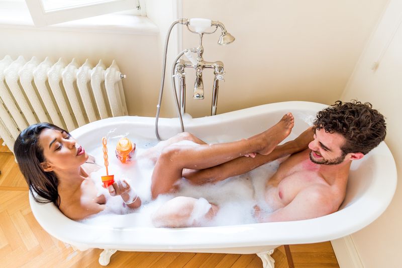 Heureux couple rire ensemble dans le bain et faire des bulles