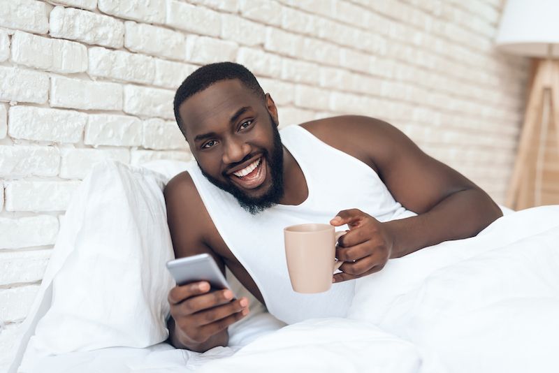 Happy man drinking coffee in bed