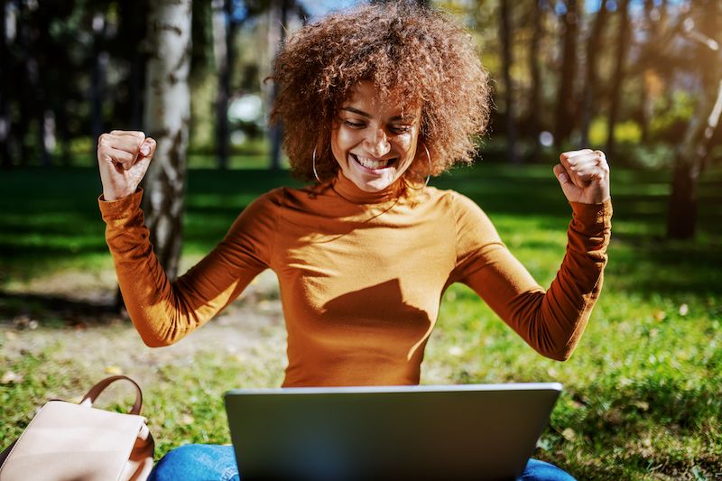 Femme assise dehors sur son ordinateur portable célébrant