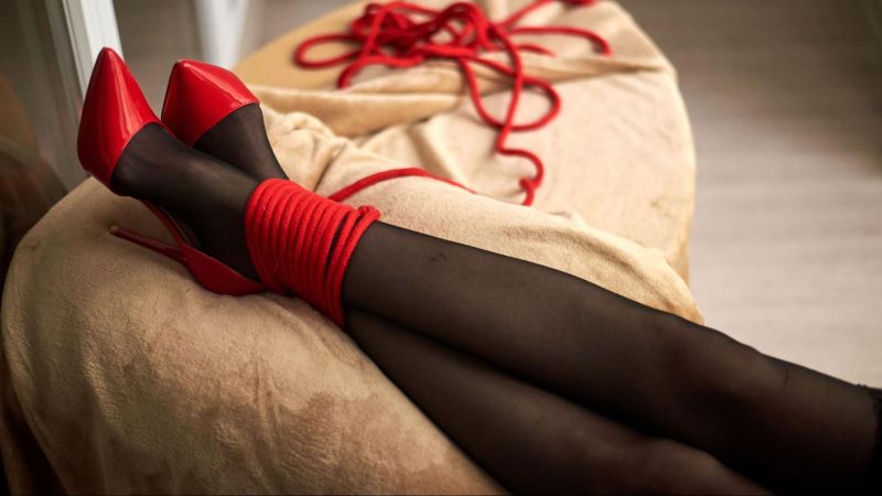 Legs and feet of woman in red heels with BDSM rope
