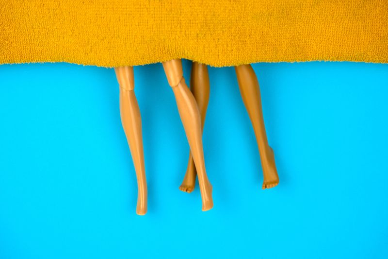 Legs of plastic dolls under blanket blue background