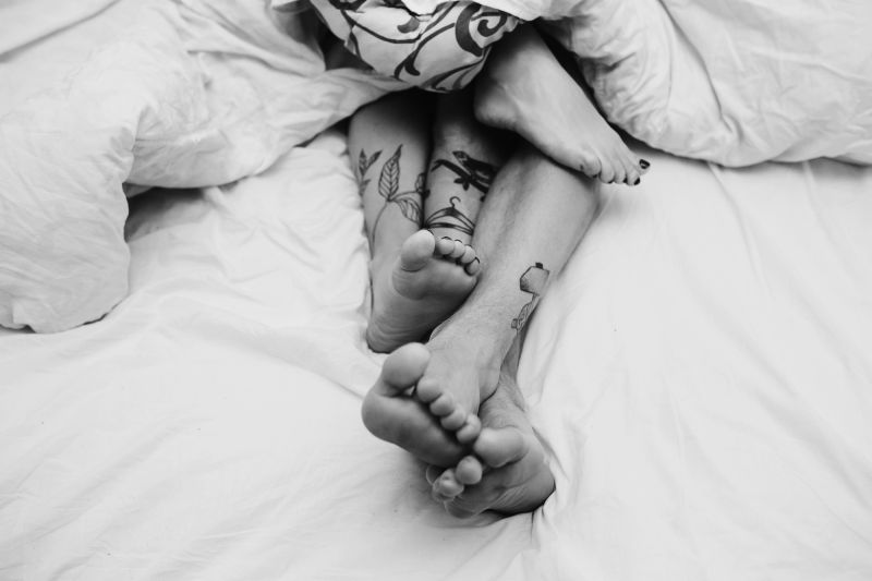 Legs of tattooed couple in bed black and white