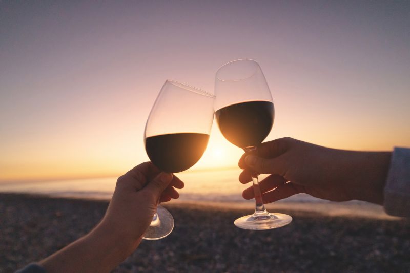 Mains tenant du vin rouge au coucher du soleil