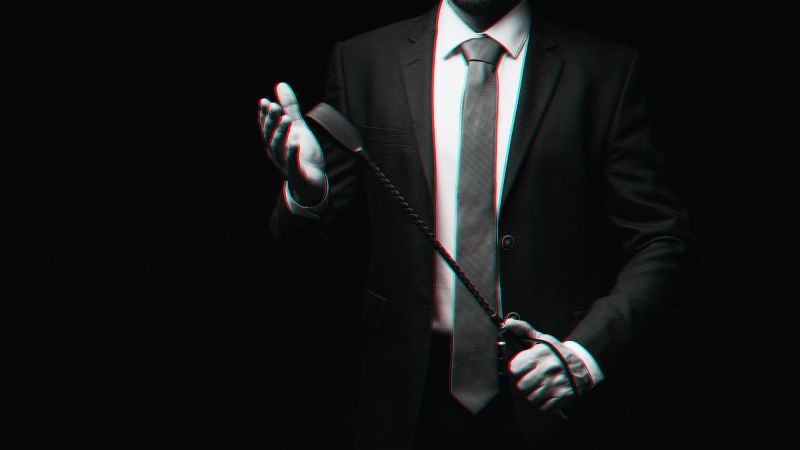 Male dom in suit holding leather whip