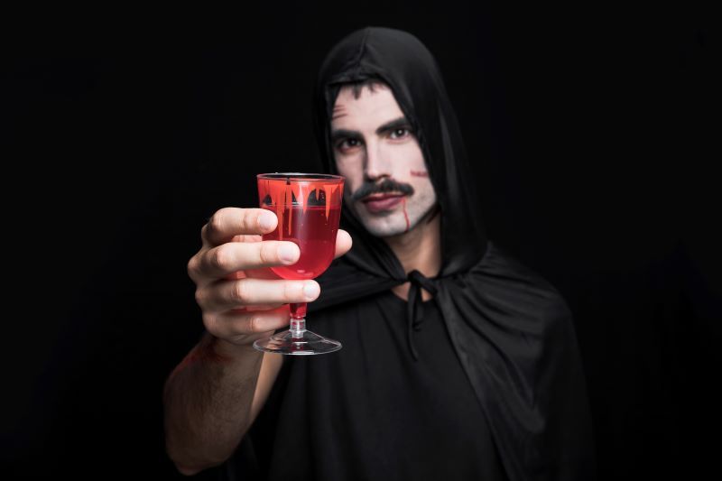 Man dressed as vampire holds up a drink