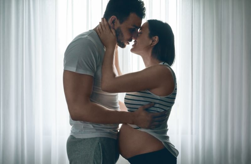 Man embracing and kissing pregnant partner at home