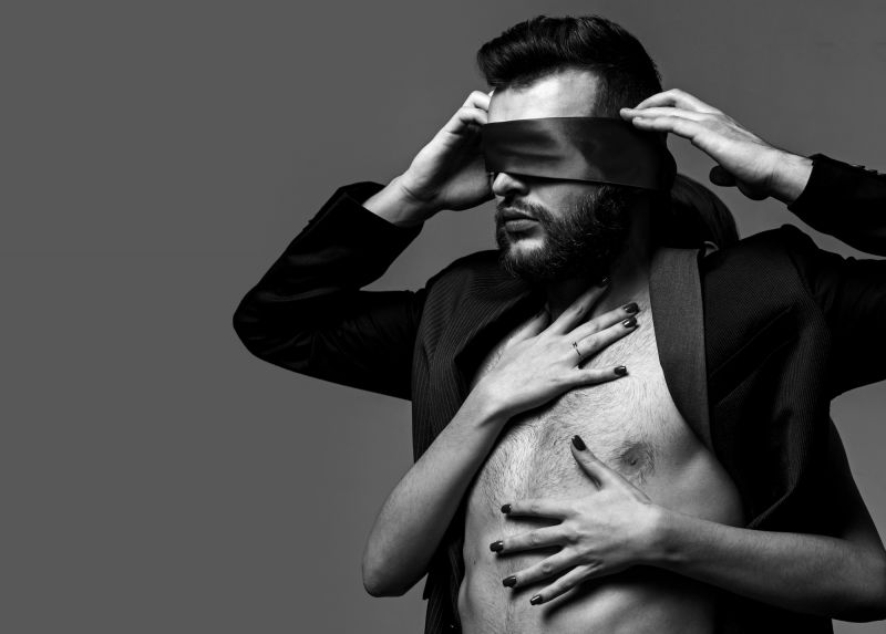 Man with ribbon blindfold and female hands on chest