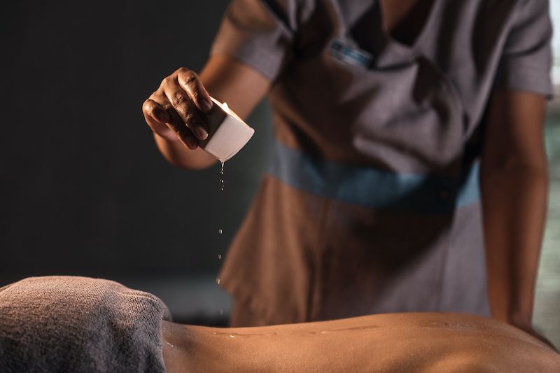 Masseur drips candle wax onto the back of a person