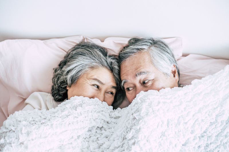 Older couple smiling under duvet together
