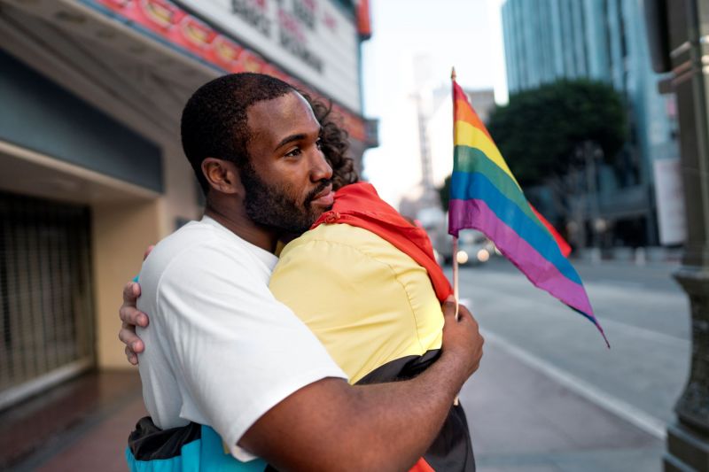 People hugging with rainbow flag at pride march