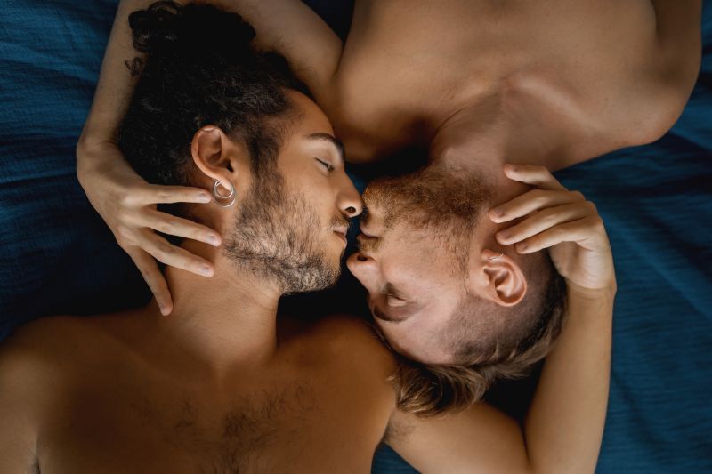 Queer topless couple embracing in bed