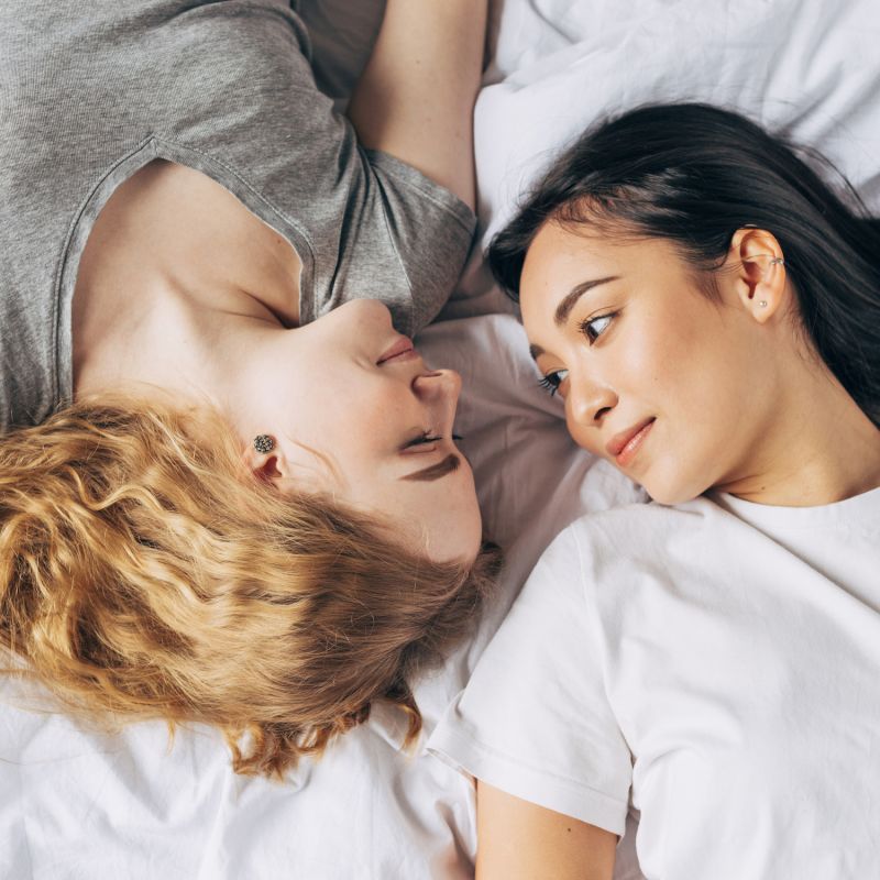 Queer couple look adorably at each other in bed