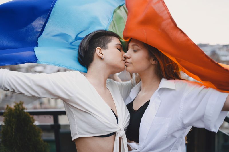 Queer couple kissing and waving LGBTQ flag