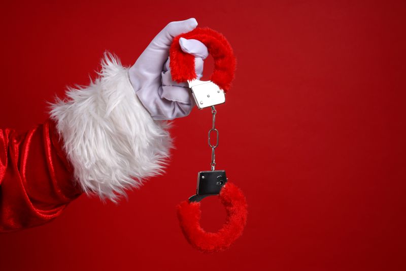 Santa hand holding red fluffy handcuffs