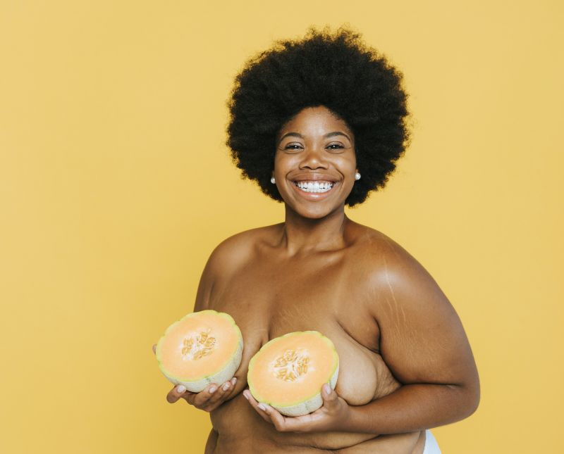 Smiling woman holding melon over breasts