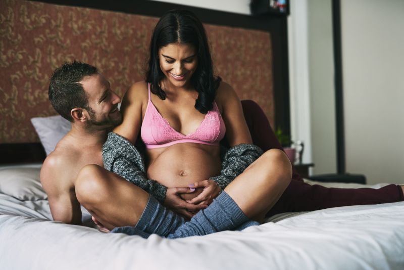 Smiling pregnant couple in bed in underwear