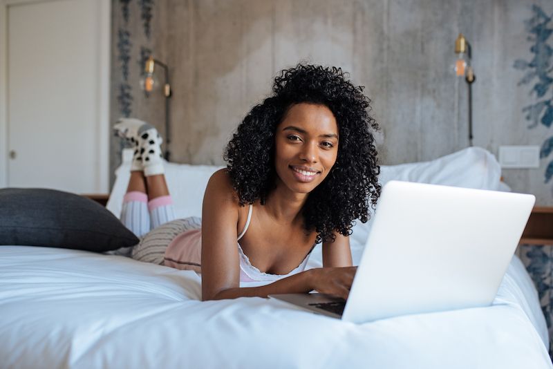Femme souriante sur son ordinateur portable au lit